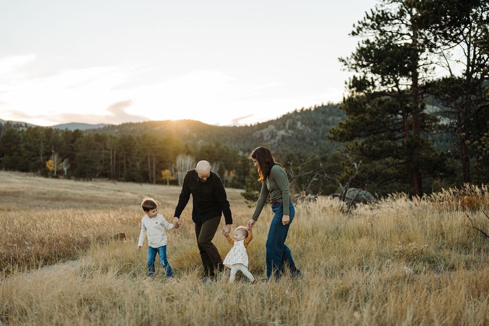 Scenic family walk along golden hillside trail during sunset with mountains and trees in background.