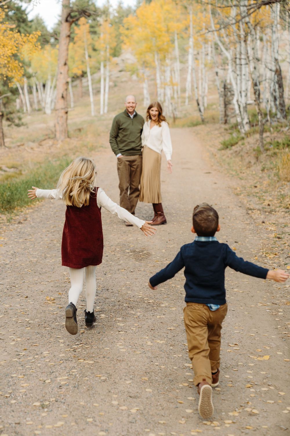 A family walking together on a dirt trail through golden aspen trees during autumn.