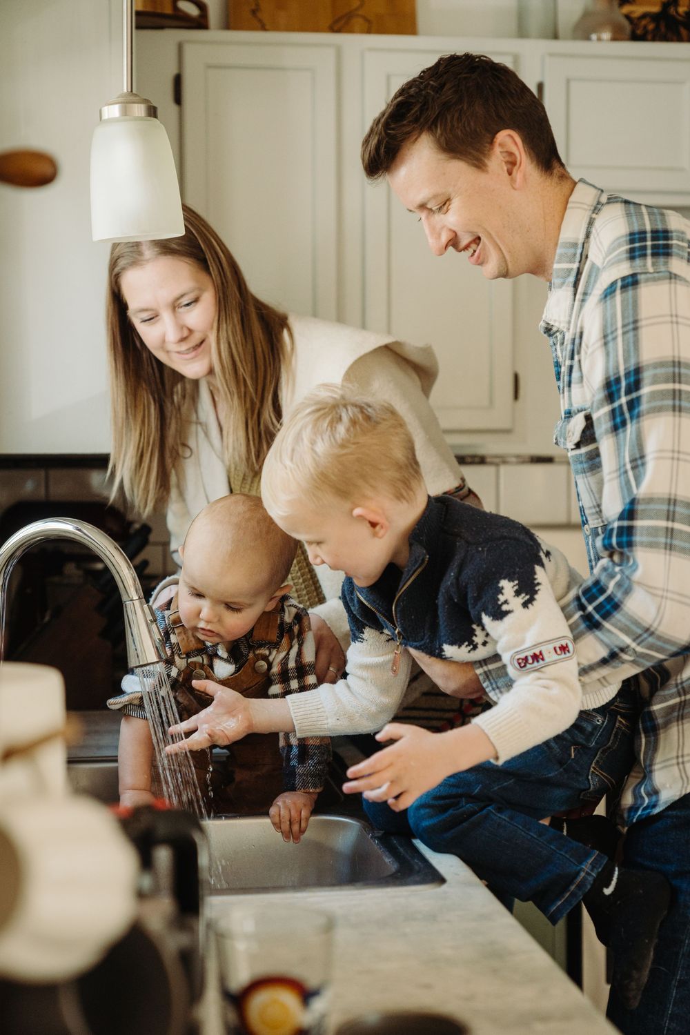 A family washes dishes together at the kitchen sink, smiling and bonding during the everyday household chore.