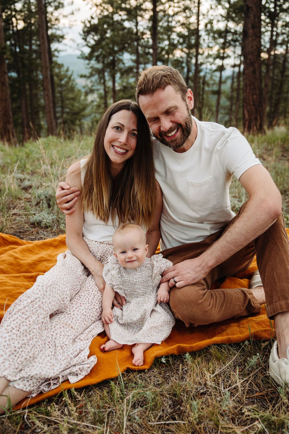 Family relaxing together on orange blanket during outdoor forest photo session in pine woods.