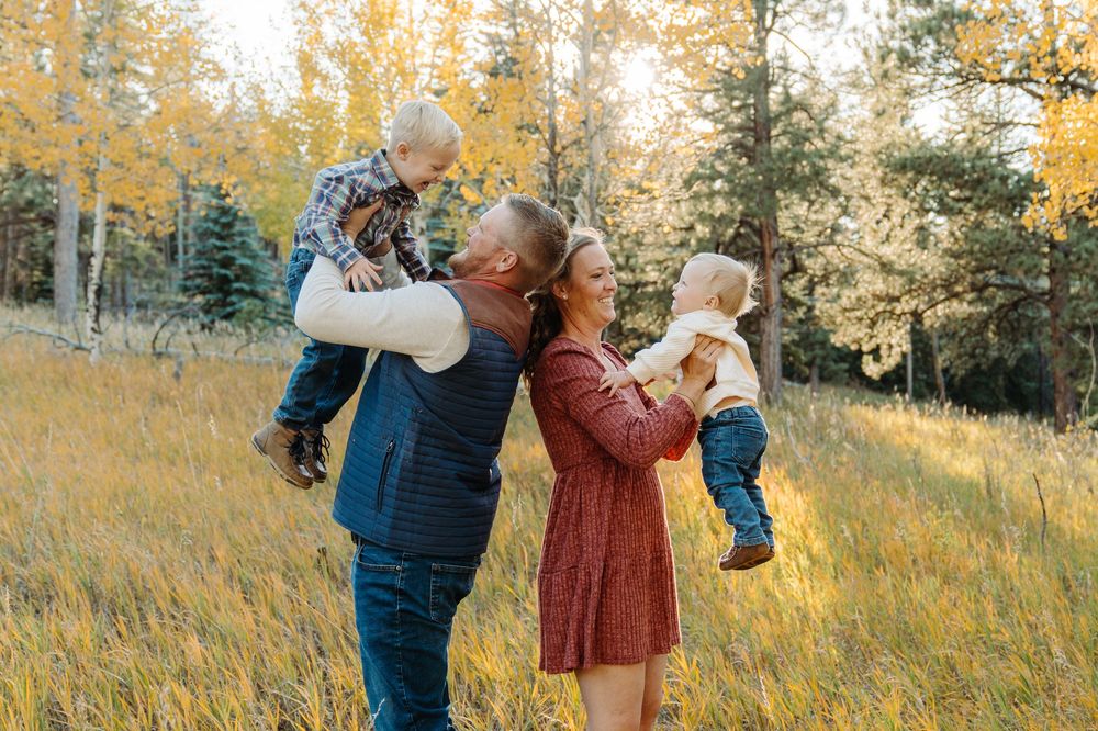 Couple embraces in a golden autumn field at sunset with tall grass and trees in the background.