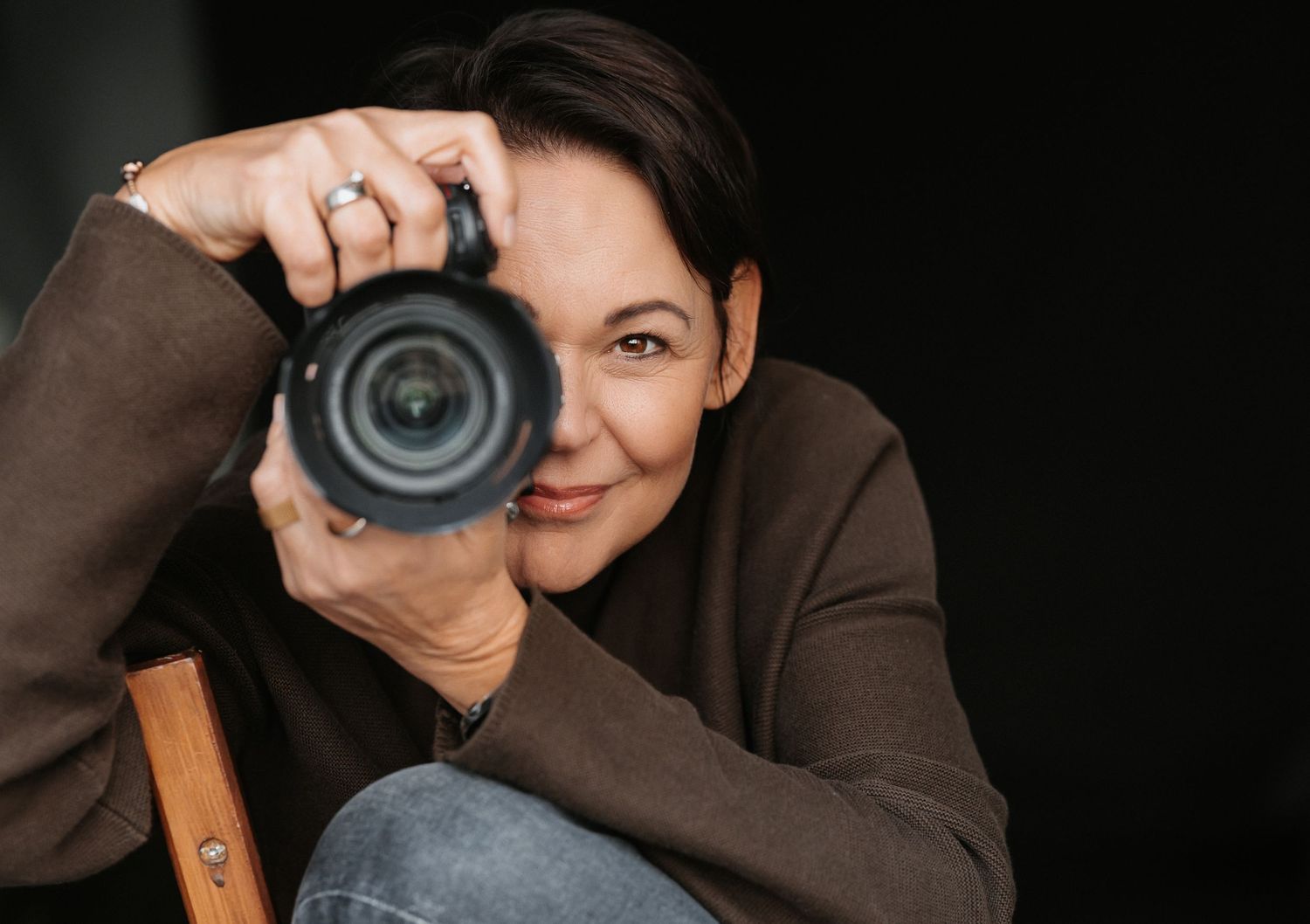 Fotografin hält Kamera vor das rechte Auge und blickt direkt in die Linse- authentisches Portrait einer professionellen Fotografin.