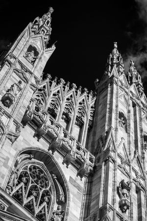 Gothic cathedral facade with ornate spires and decorative stone carvings photographed in dramatic black and white.