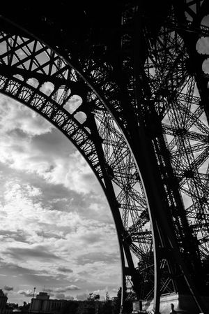 Silhouetted steel arches of the Eiffel Tower frame dramatic cloudy sky in black and white sequence.