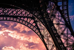 Silhouetted Eiffel Tower arch detail against a dramatic pink and purple sunset sky in Paris, France.