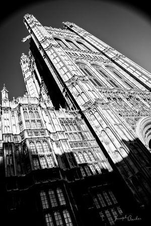 Dramatic black and white photograph of the Houses of Parliament towers in Westminster shot from below against dark sky.