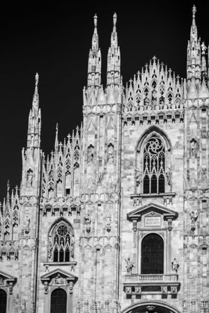 Dramatic black and white architectural detail of Milan Cathedral's Gothic facade with ornate spires and rose window.