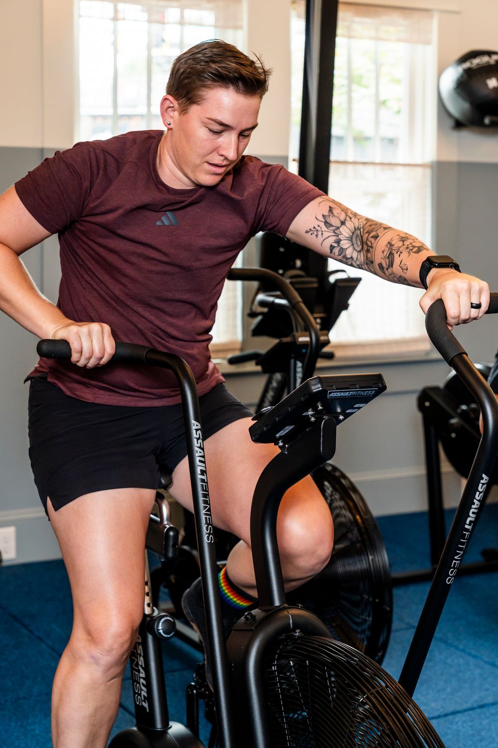 Fit person with tattoo sleeve working out on a black exercise bike in a home gym setting.