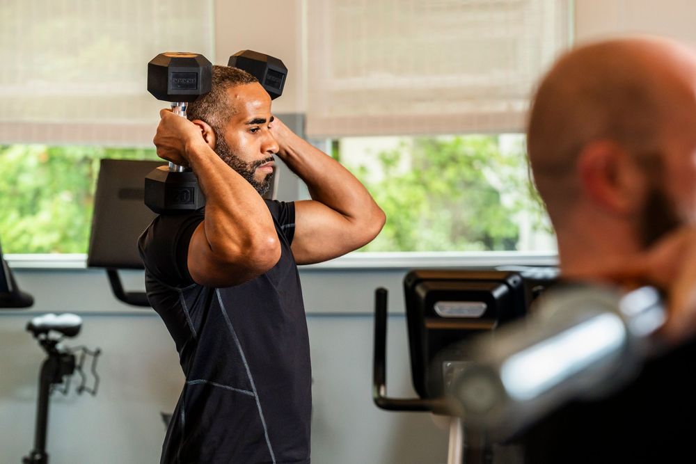 Person doing concentration curl exercises with dumbbells at a workout station in a gym.