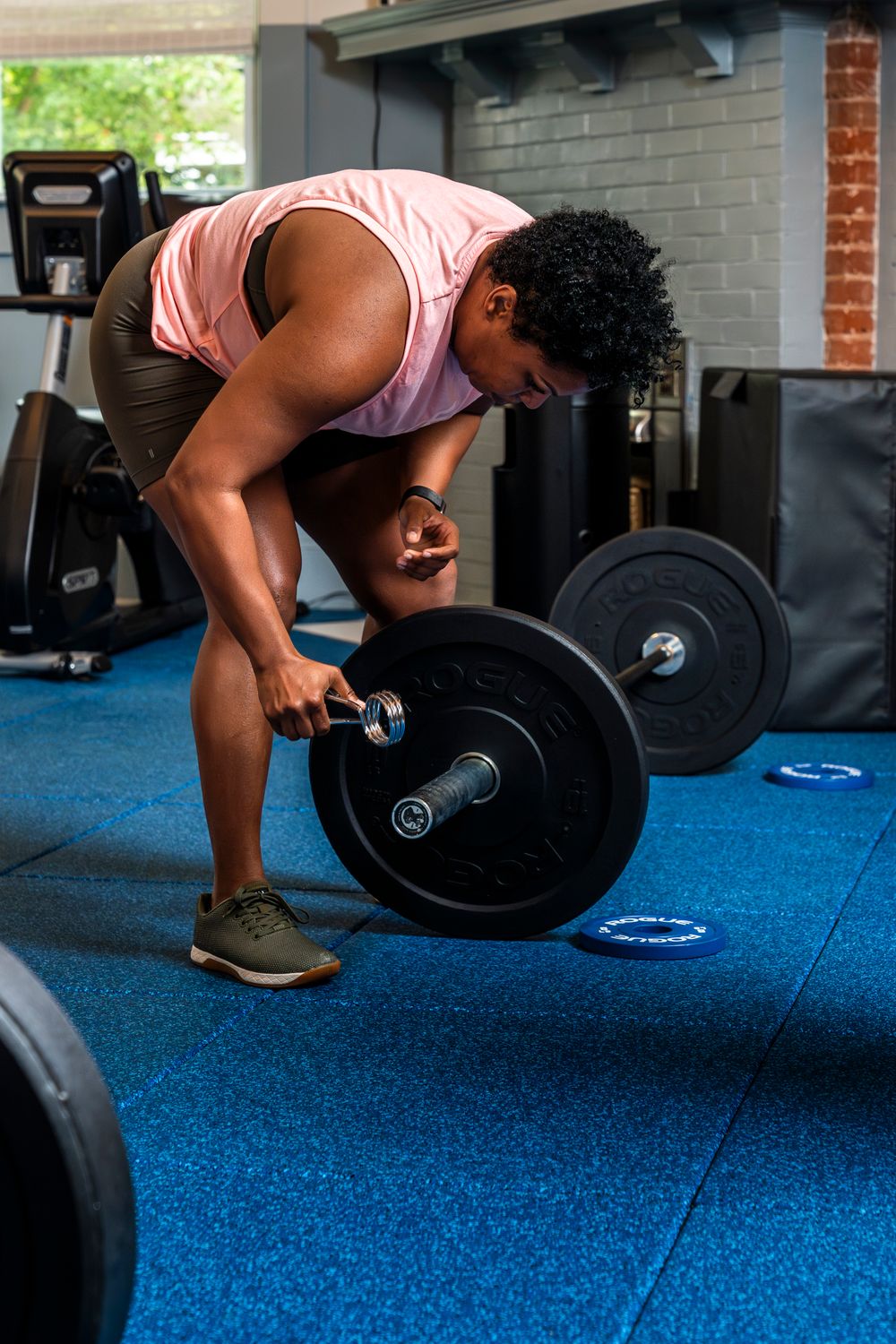Person performing a deadlift exercise with proper form on bright blue gym flooring with a heavy barbell.