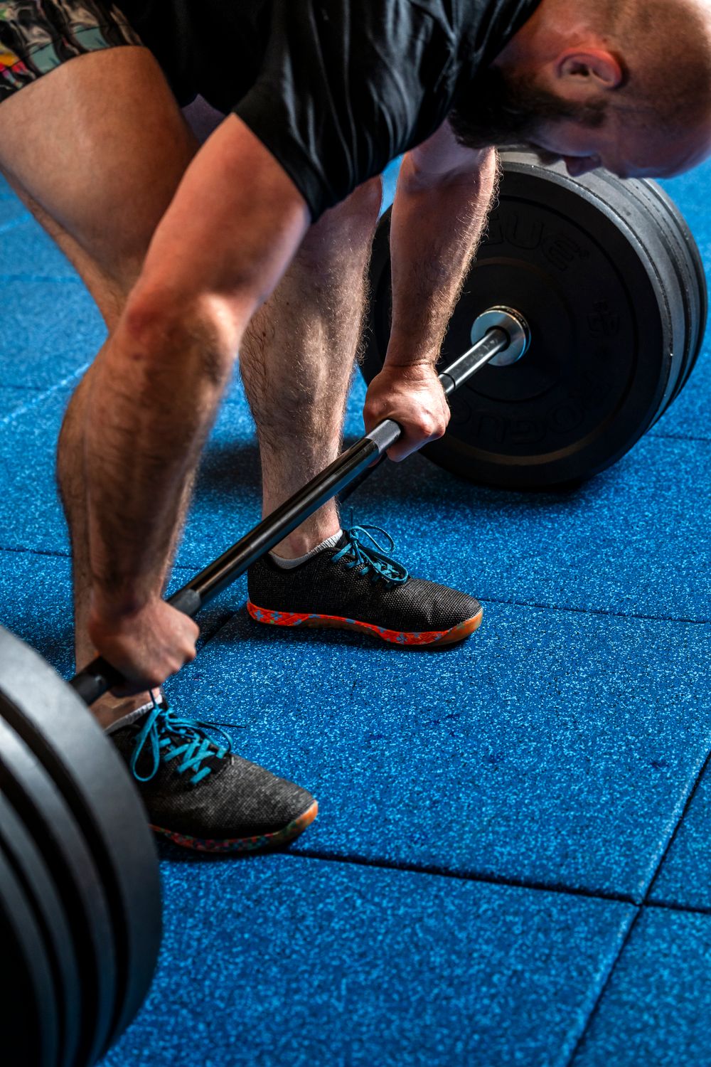 Close-up of person gripping a barbell on blue gym flooring during weightlifting workout.