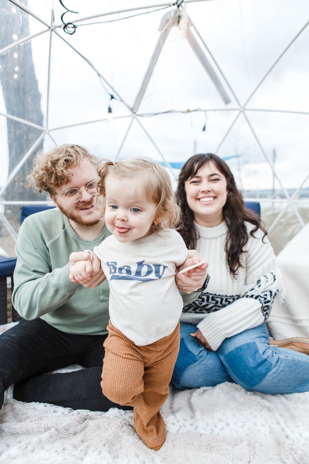 Three people sit together smiling in a geodesic dome interior with white cushions and light filtering through.
