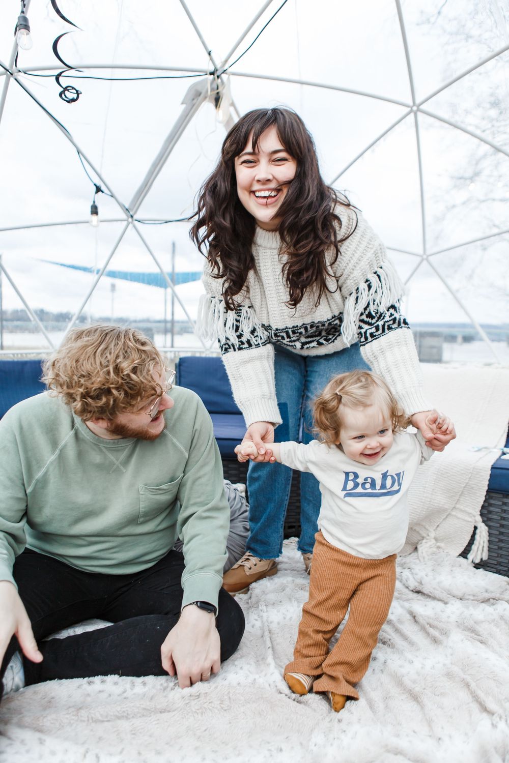 Parent and toddler share playful winter moments against white geodesic dome backdrop in family photoshoot.