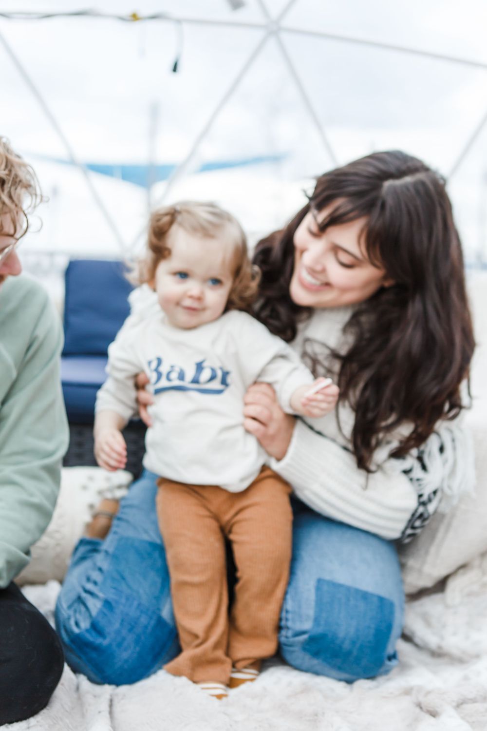 A toddler in a white shirt and khaki pants sits between two adults on a couch, sharing a happy moment together.
