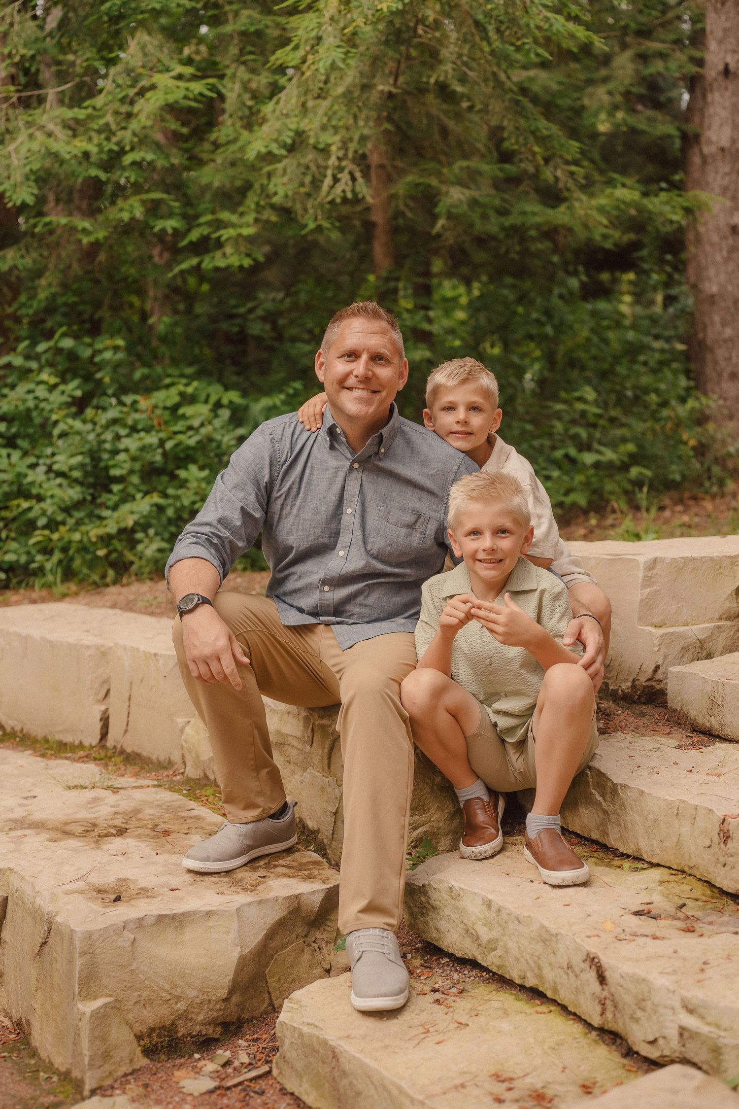 Family members sitting together on stone steps surrounded by lush green forest scenery.