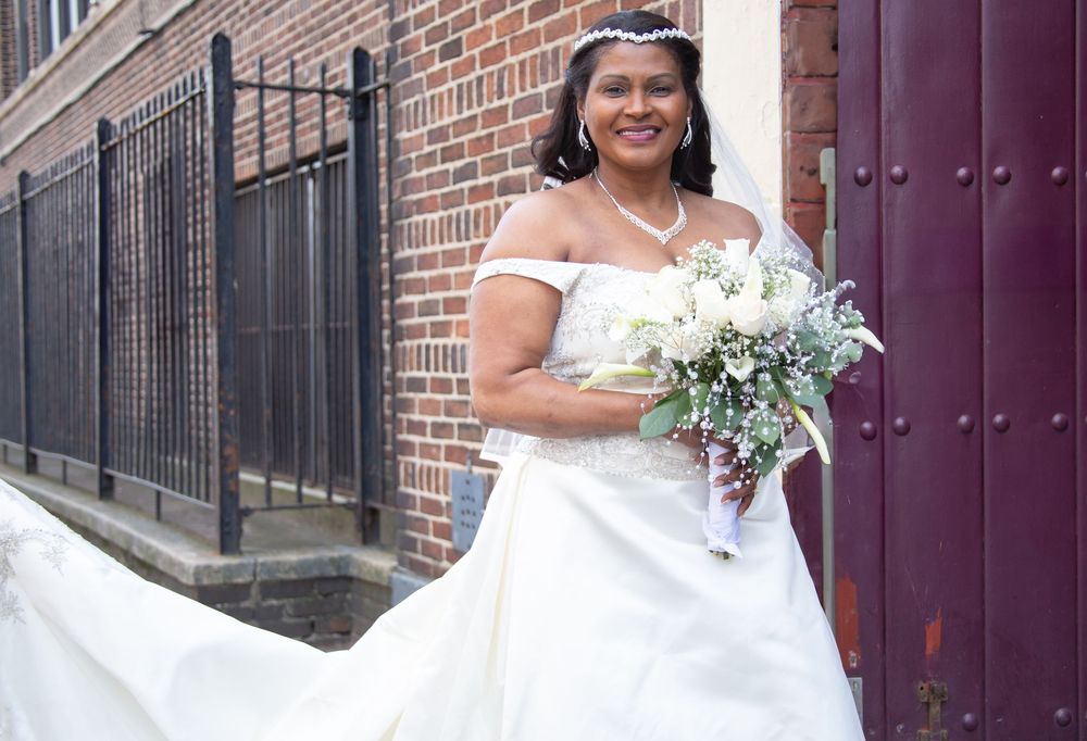 A bride in a flowing white wedding gown poses with a bouquet against a brick wall and purple door.