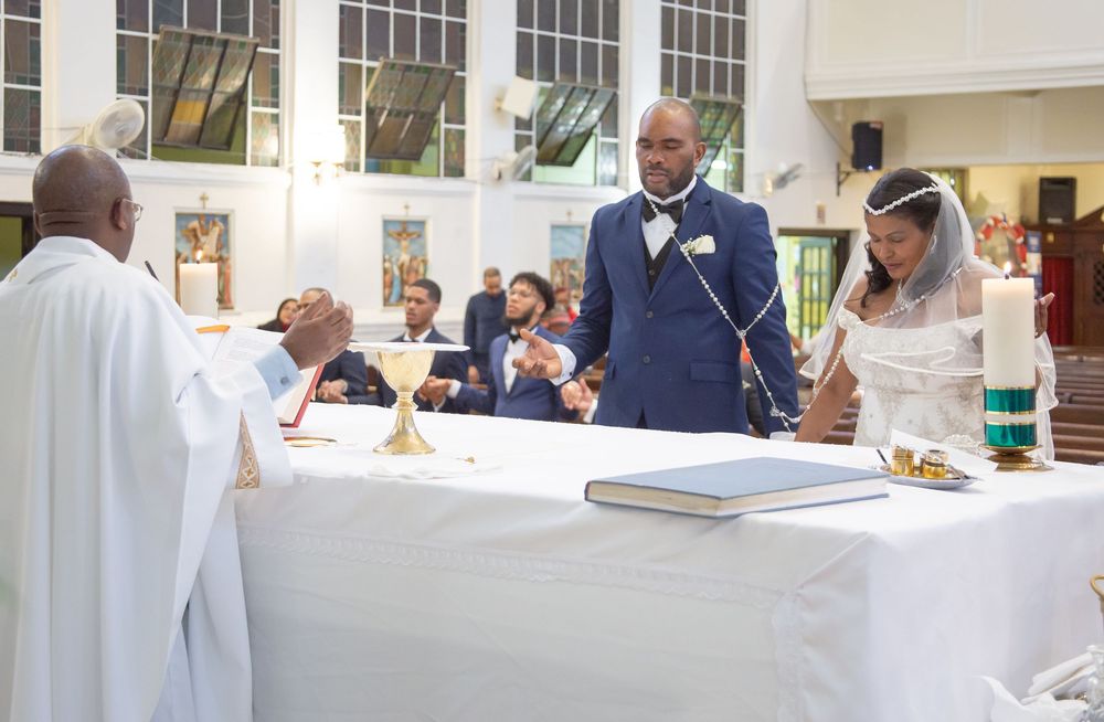 A couple stands at the altar during their wedding ceremony while guests observe from their seats in a church.