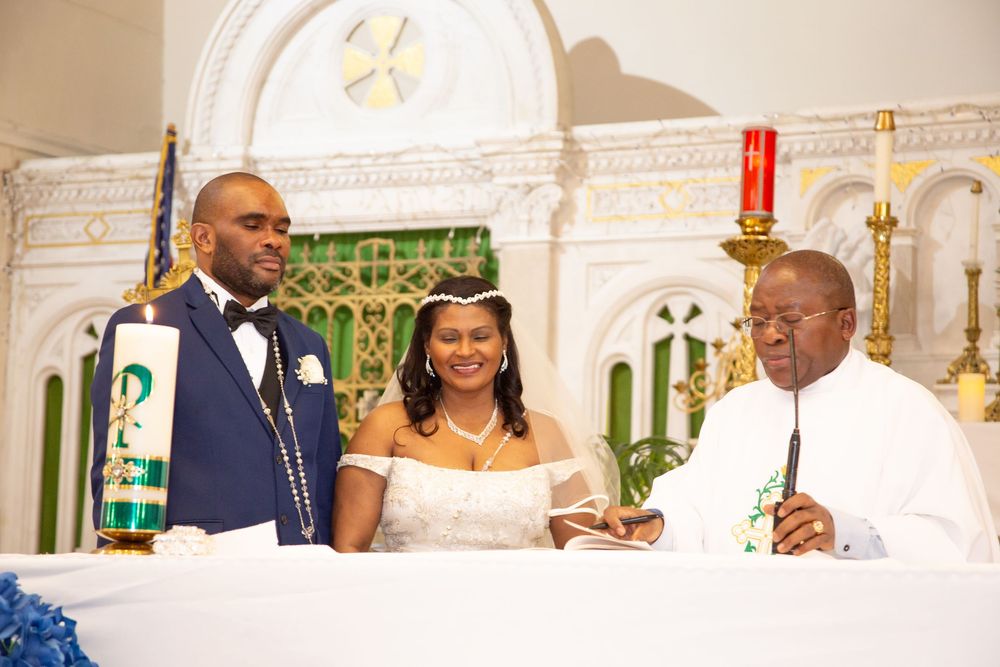 Guests gather in an elegant church interior with ornate white decor and arches during a formal ceremony.