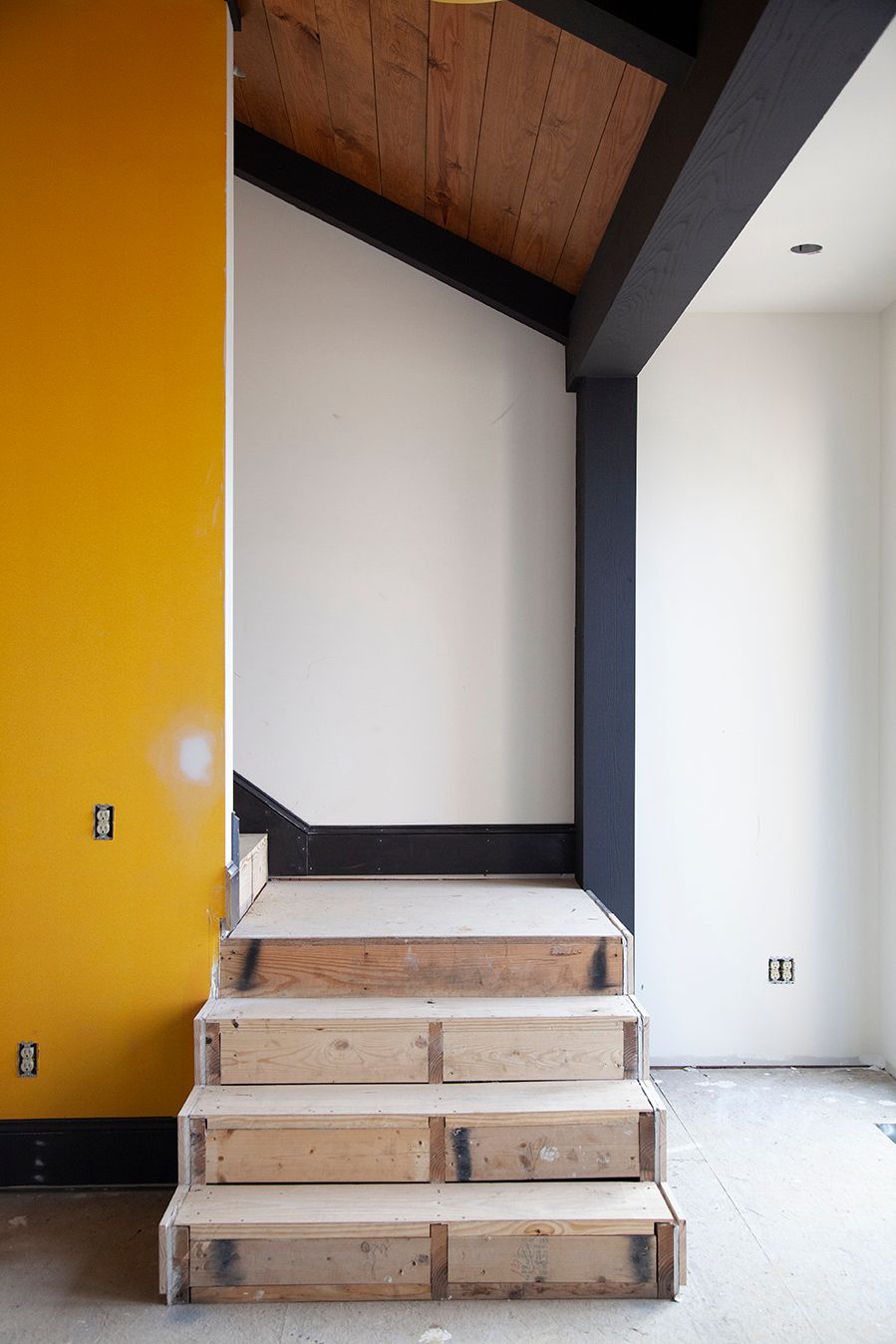 Interior room with yellow accent wall and wooden stepped platforms under a slanted ceiling.