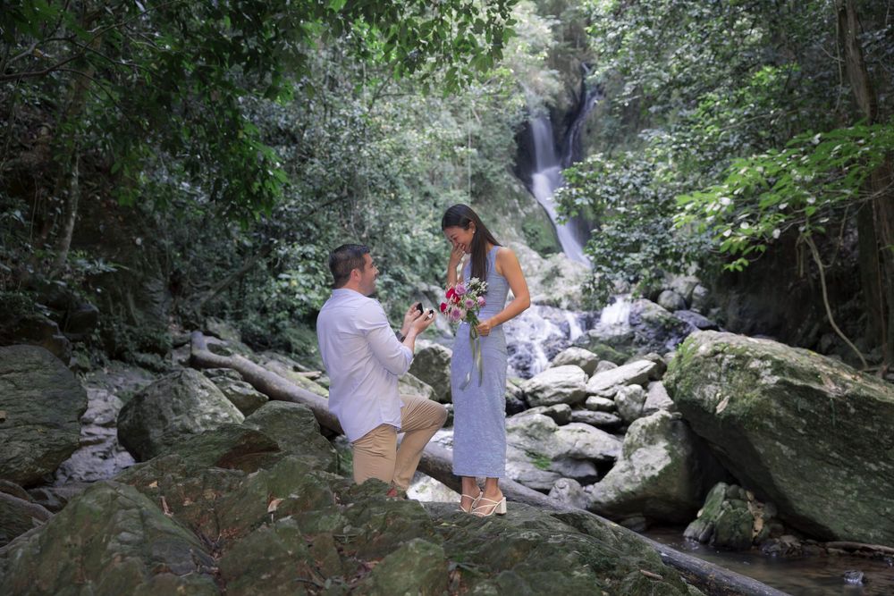 A couple shares a special moment on rocky terrain with a cascading waterfall in the lush forest background.
