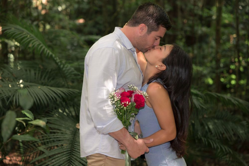 A tender moment shared between a couple in white attire embracing in a lush green tropical garden setting.