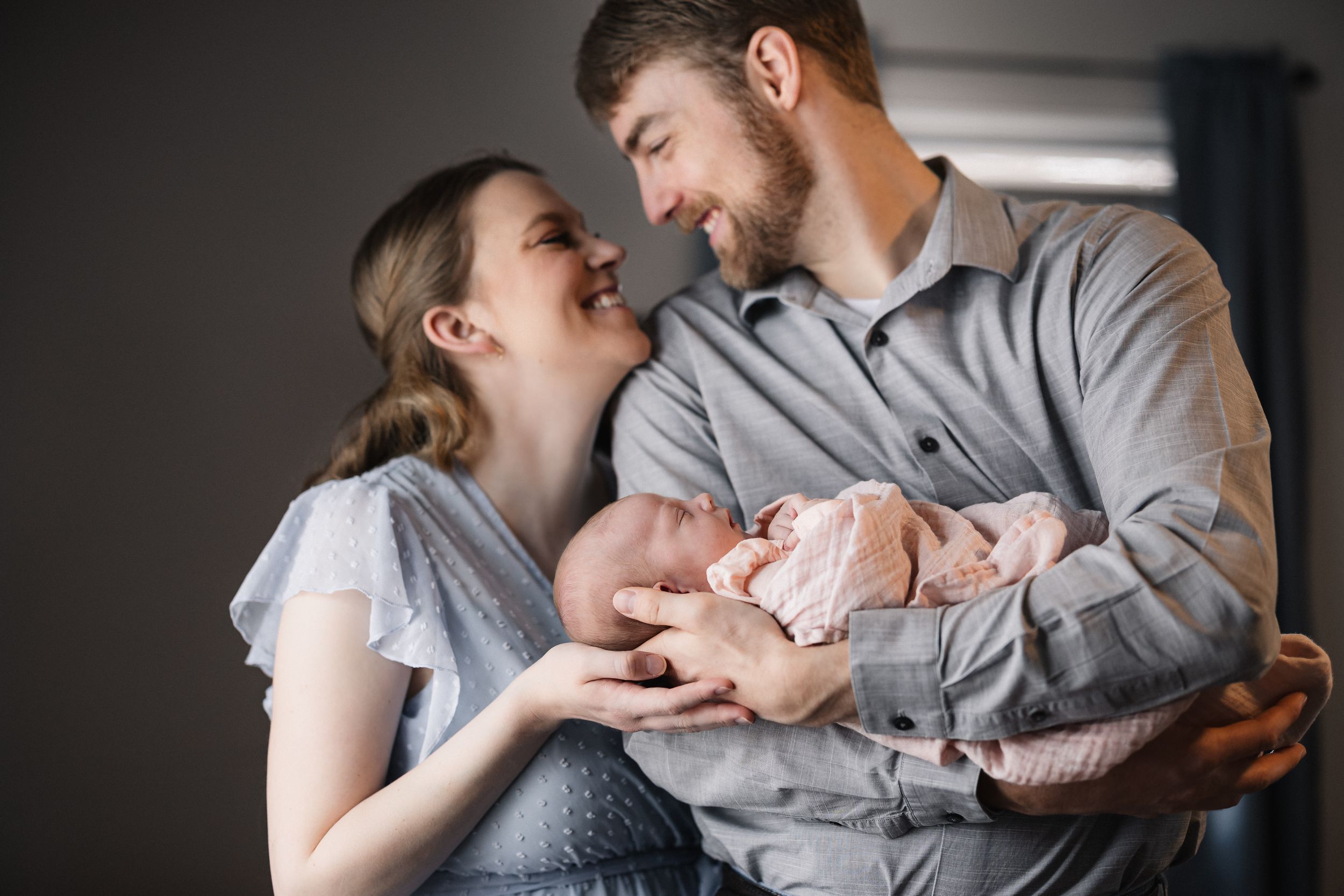A couple shares an intimate moment while holding their newborn baby wrapped in a soft knit blanket.