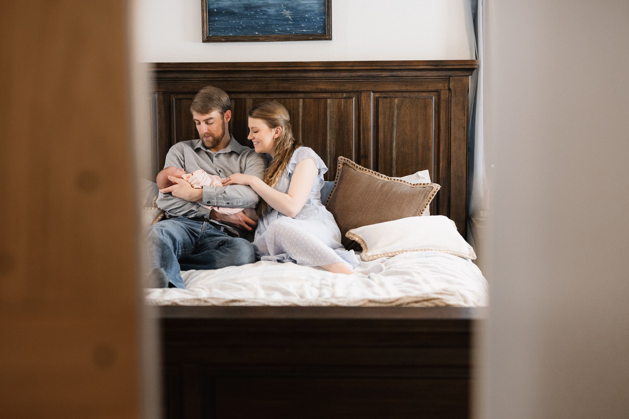 Couple sitting on bed with dark wood headboard looking at something together in a cozy bedroom setting.