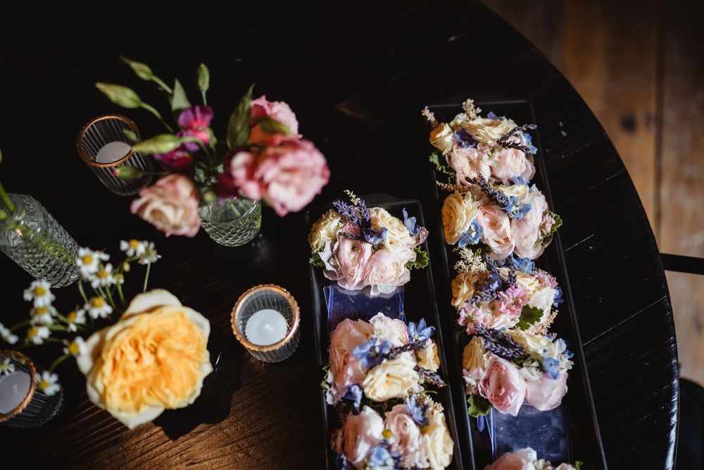 A close-up view of delicate floral arrangements and silver teapots on a rustic dark wooden surface.