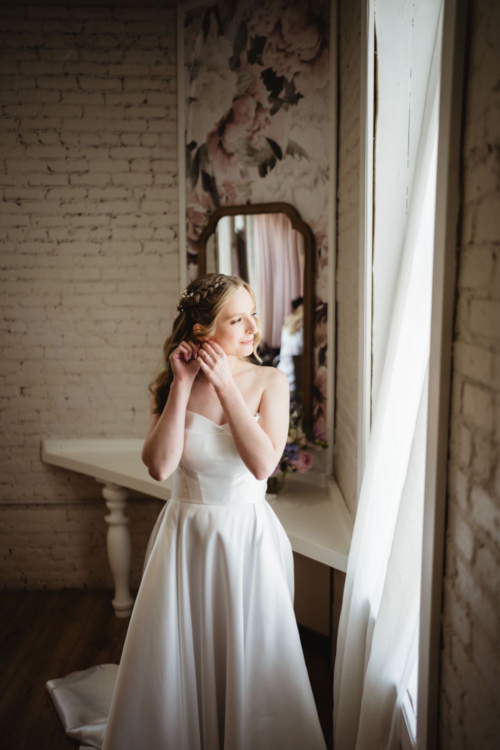 Light streams through windows in an elegant white room with exposed brick walls creating soft artistic portraits.