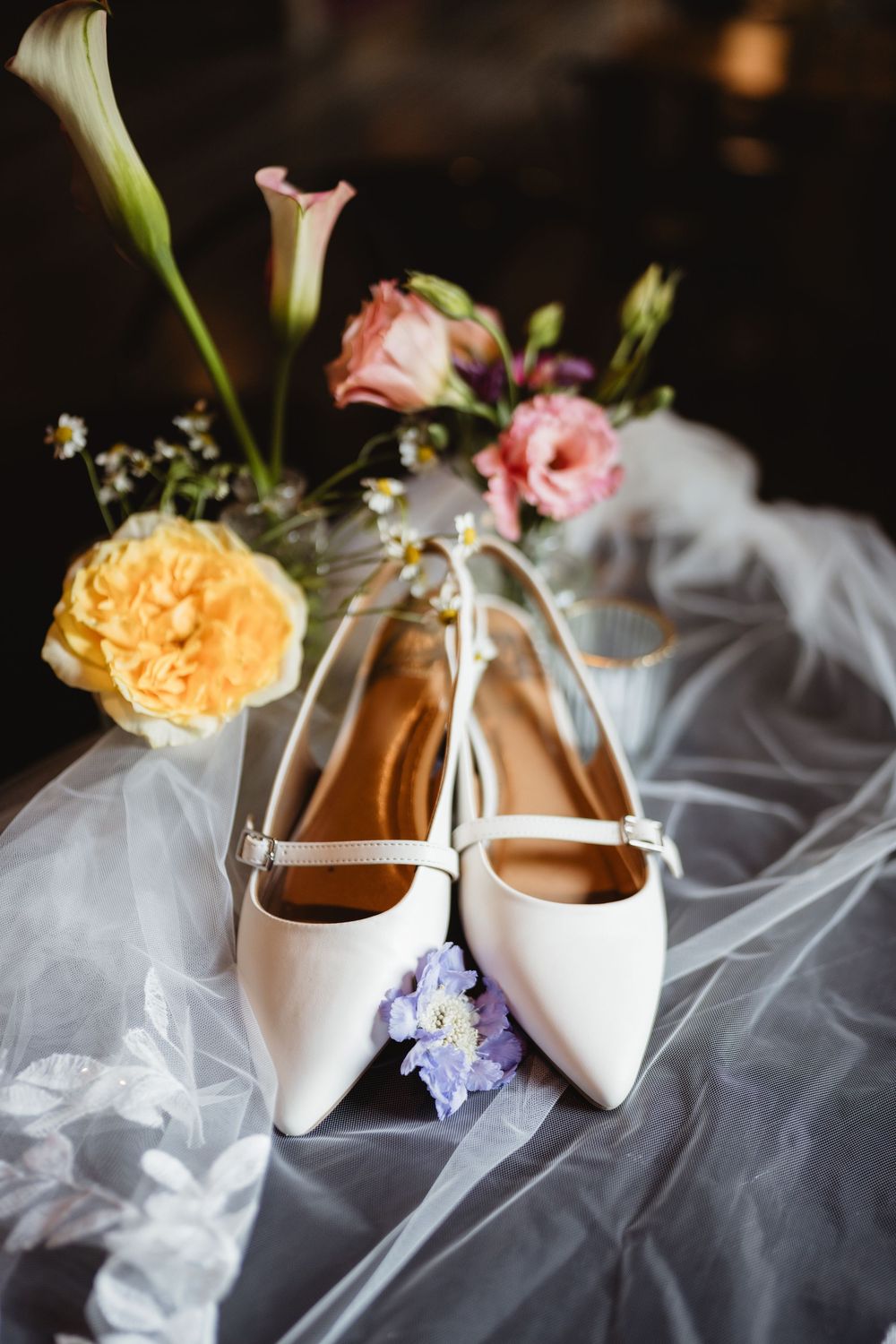White bridal heels rest on sheer fabric with delicate pink and purple floral accents.