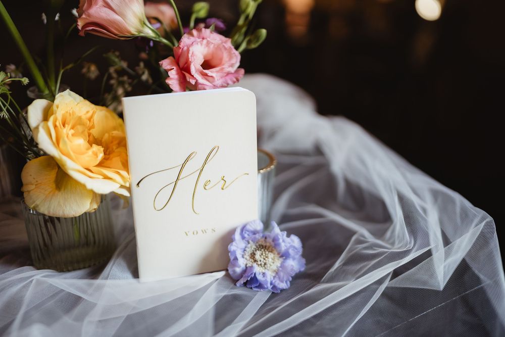 A white wedding card marked 'Hers' with pink and yellow roses on delicate tulle veil fabric.