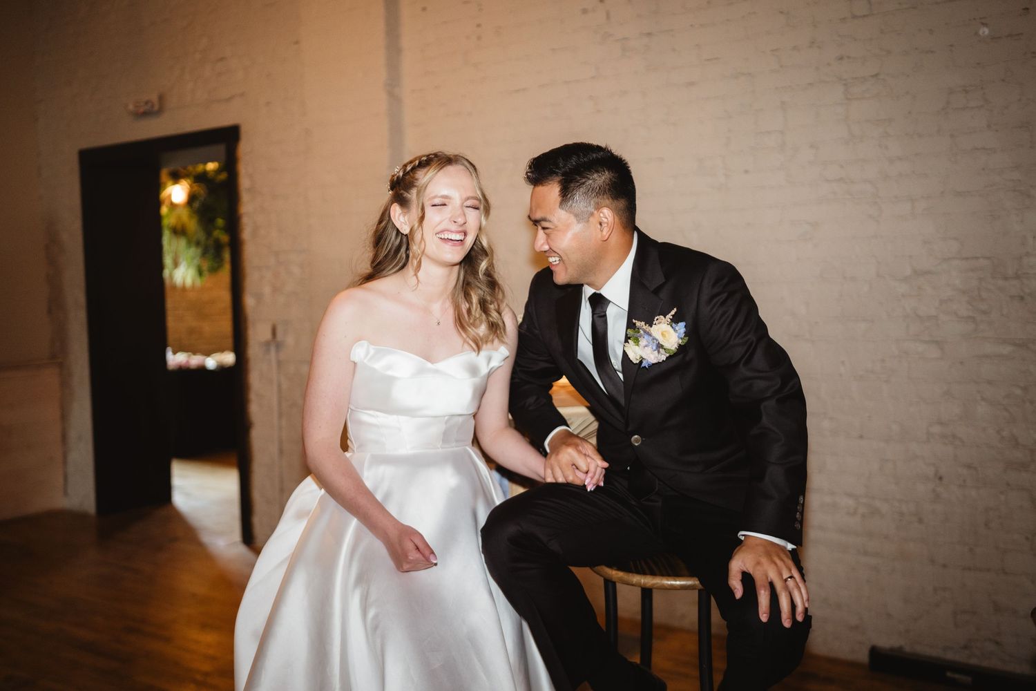 A laughing couple in formal wedding attire share a joyful moment during their reception celebration.