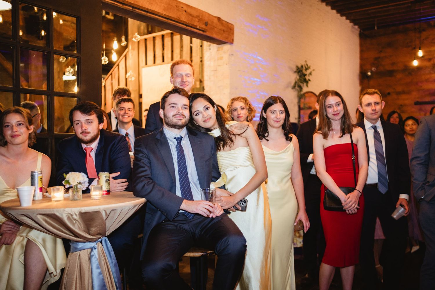 Wedding party guests dance together on a dance floor in a softly lit indoor reception venue.