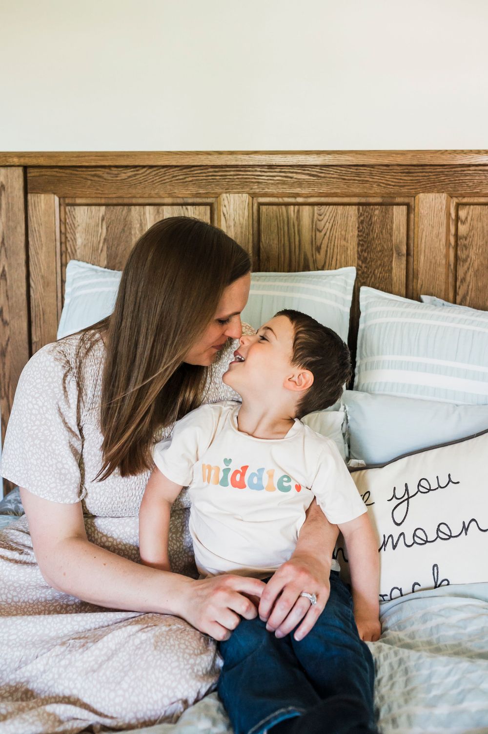 Mother and child sharing tender playful moments together while lying on bed with white pillows.