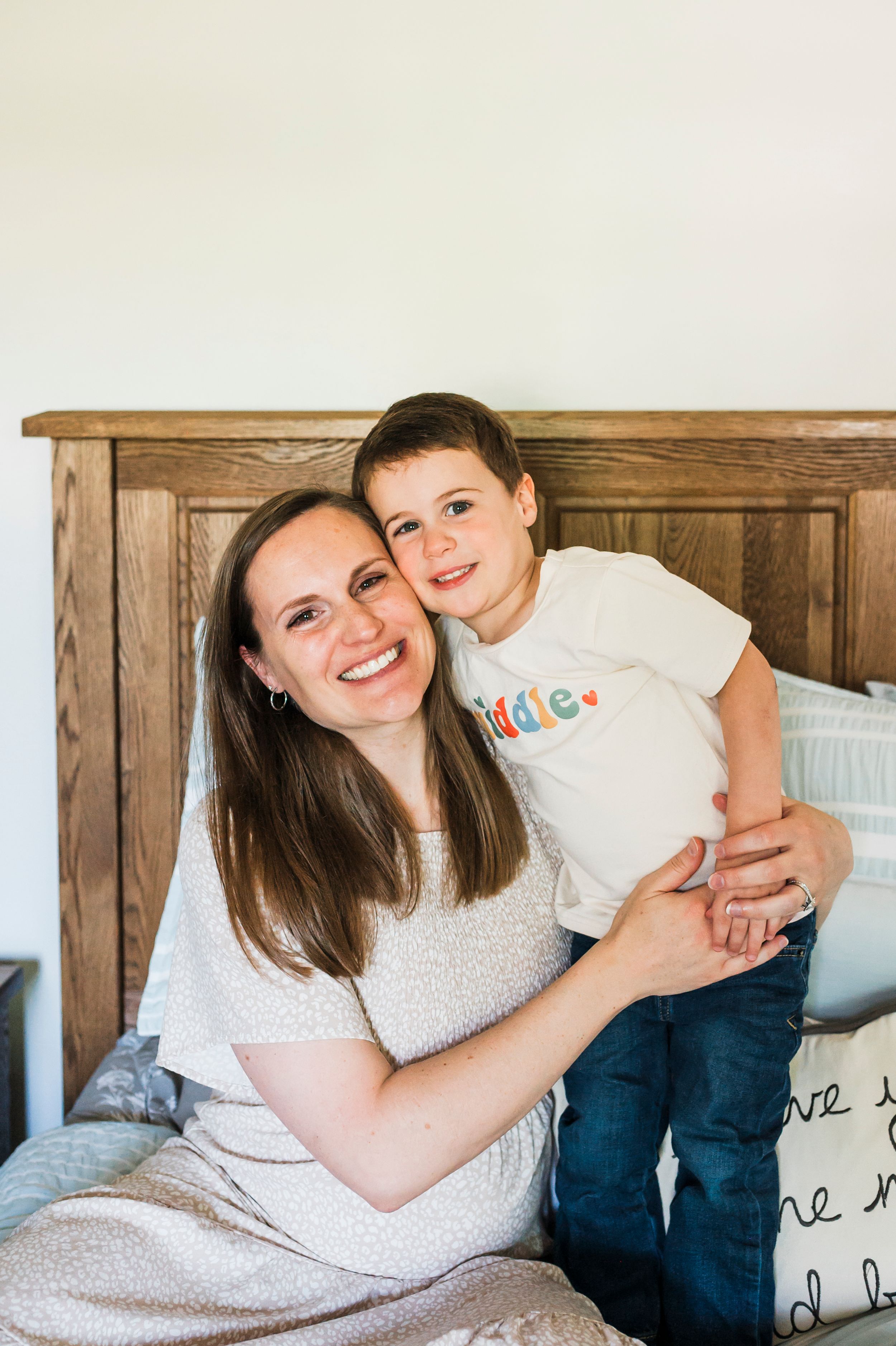 A warm family moment in front of a wooden headboard bed with decorative pillows.