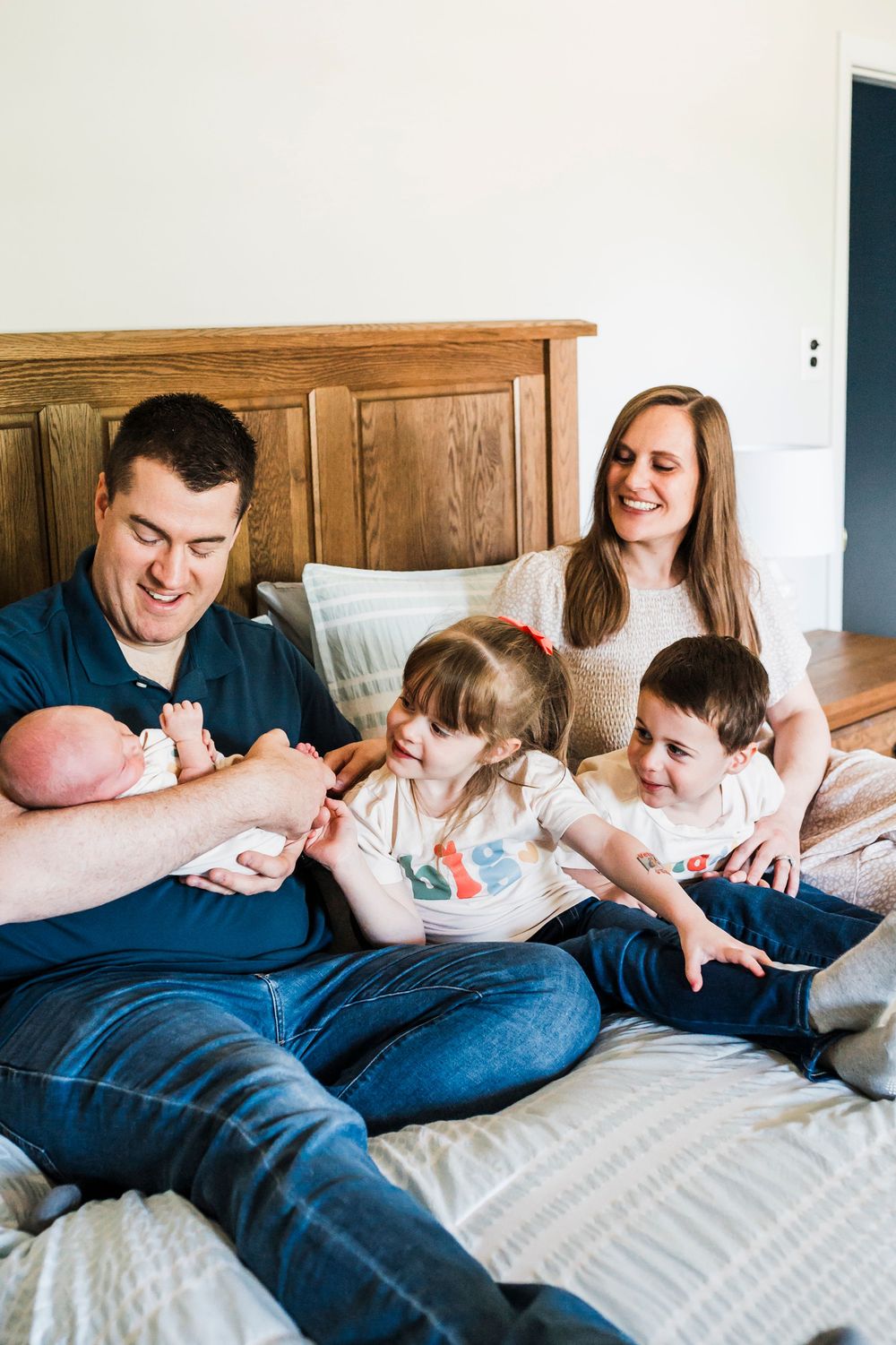Family relaxing and playing together on a cozy bed with wooden headboard in natural lighting.