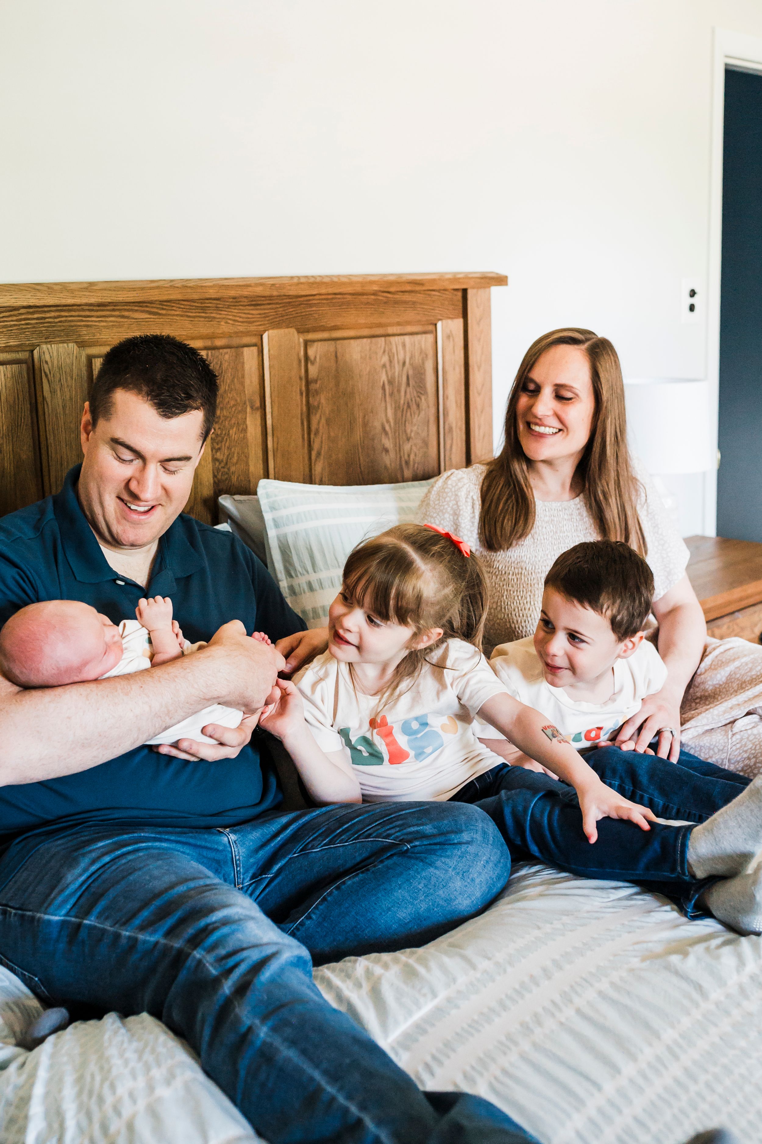 Family relaxing and playing together on a cozy bed with wooden headboard in natural lighting.