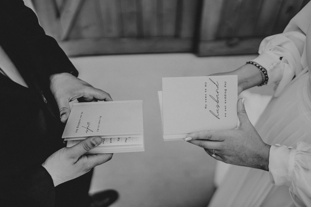 Black and white view of two people holding wedding vow cards during a ceremony preparation.