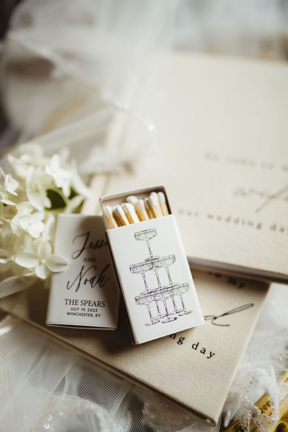 A series of elegant wedding invitation matchboxes decorated with custom monograms and floral accents on a light fabric background.