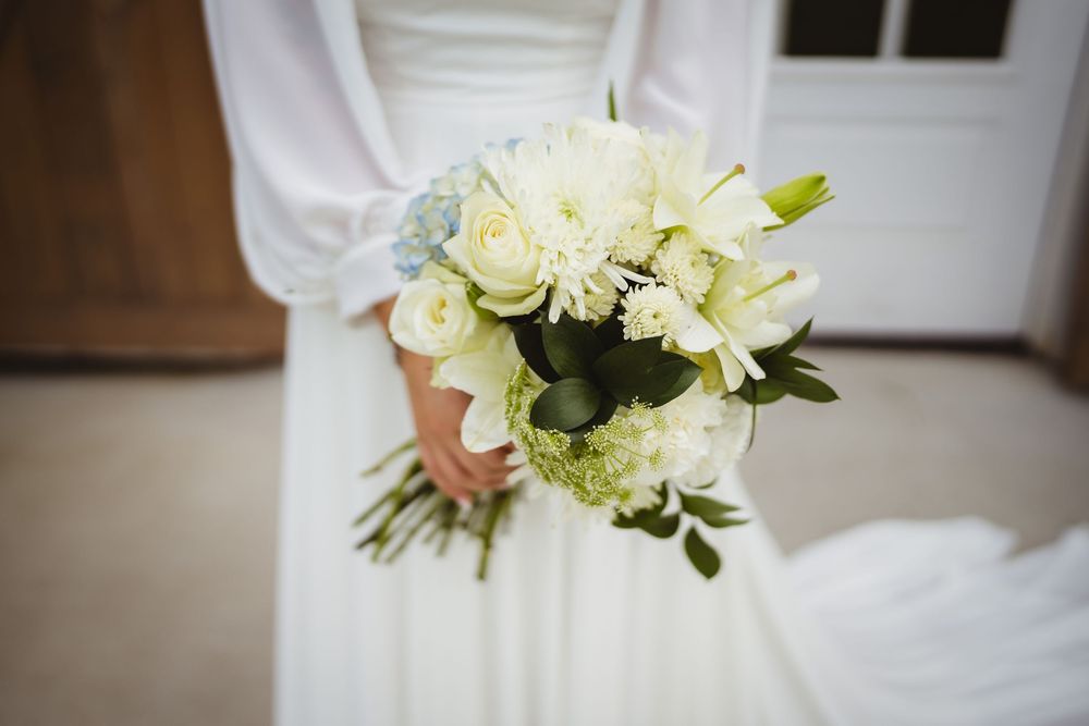 Elegant white and cream bridal bouquet with roses and mixed flowers against a wedding dress.