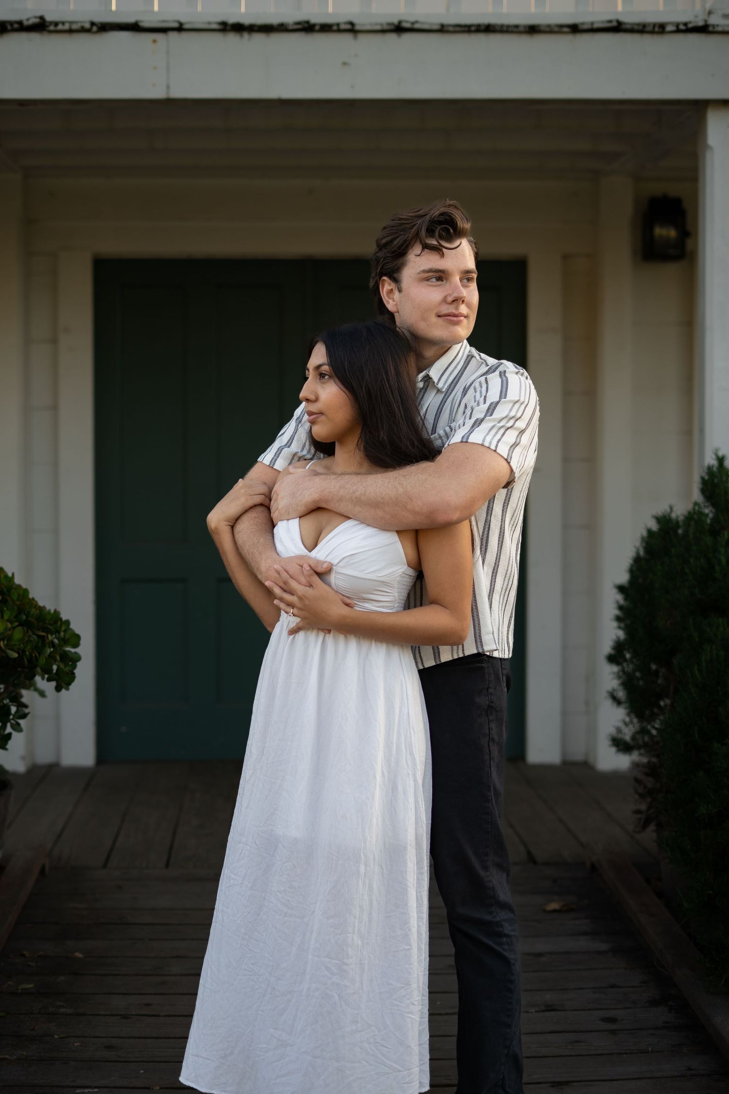 Couple embracing outside white building with green doors.