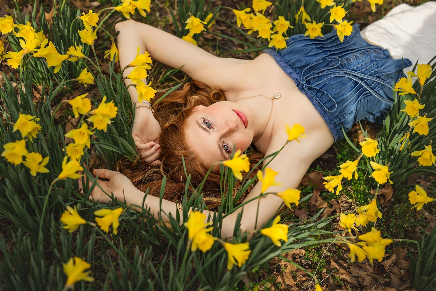 A girl lies peacefully among vibrant yellow daffodils in a spring garden setting.