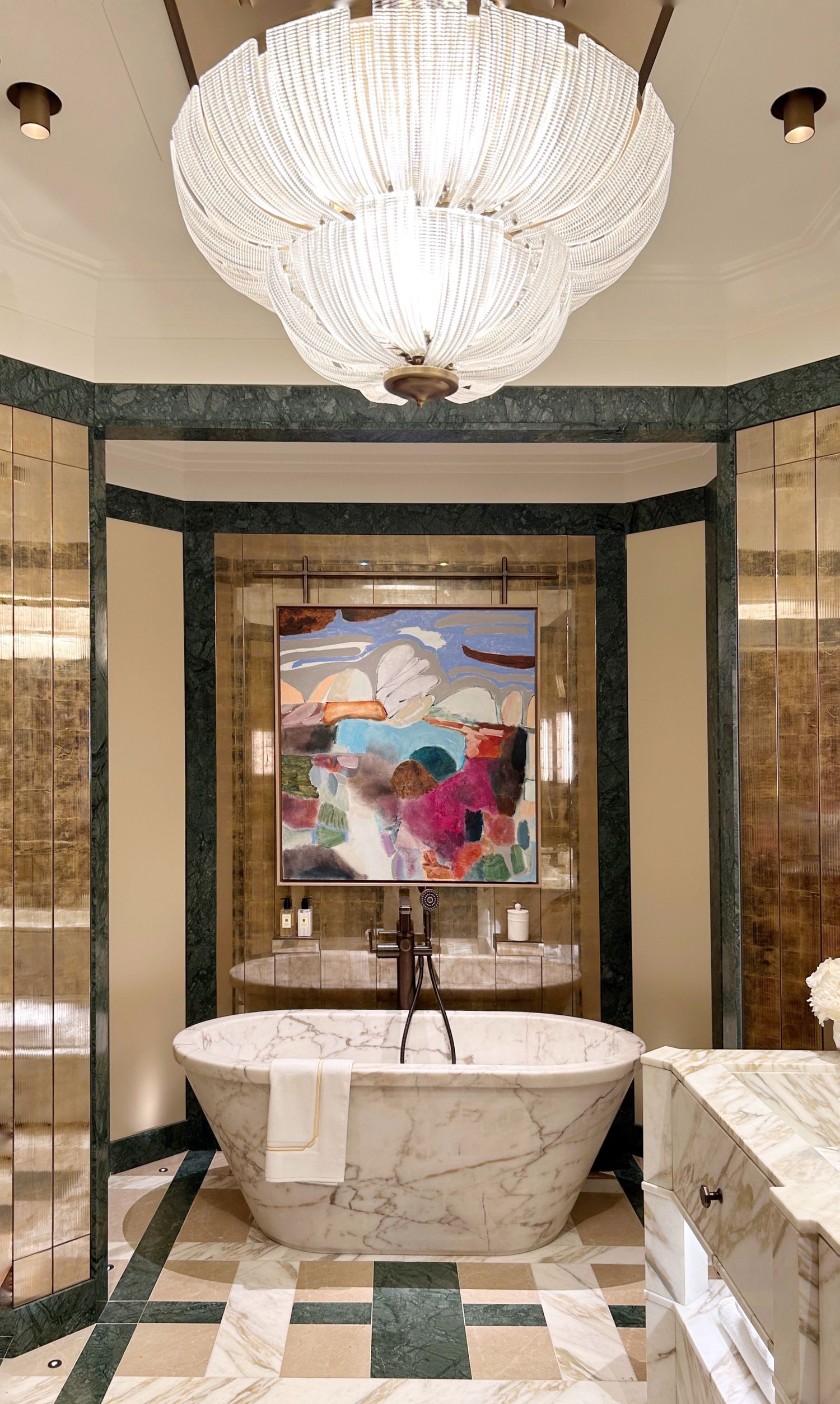 Luxurious marble bathroom  with marble  bathtub, art deco chandelier, and colourful modern artwork. Laura Hammett and Samuel Heath