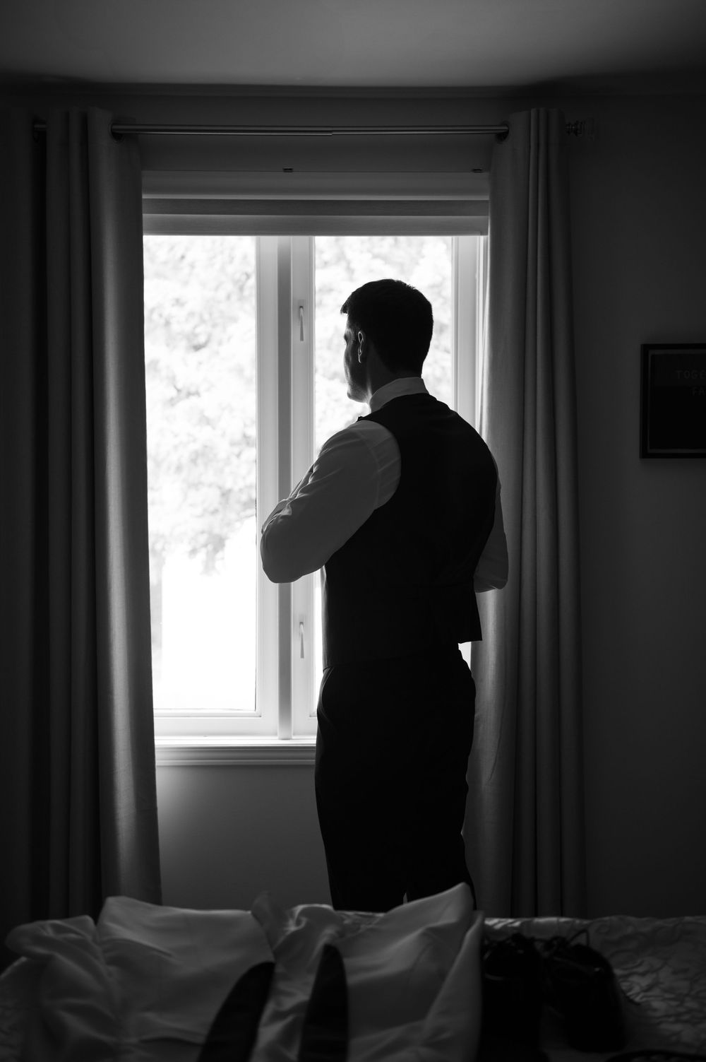 Silhouetted figure stands by bright window in dark room with curtains.