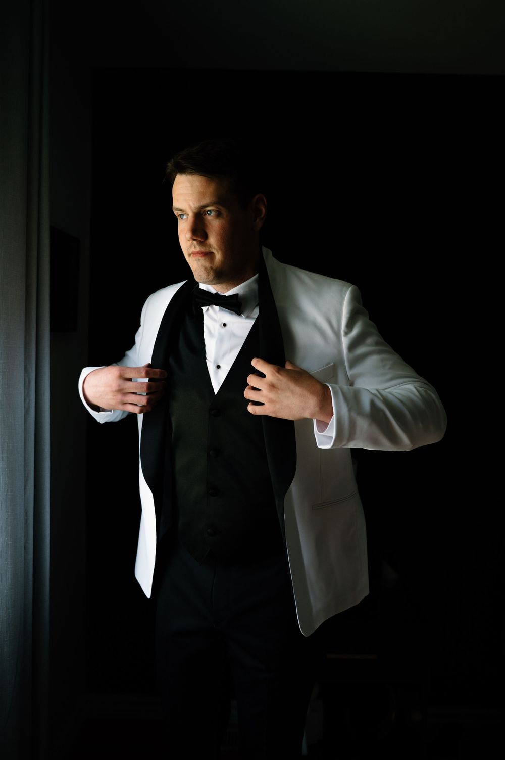 Dramatic lighting captures formal wear preparation in dark room.