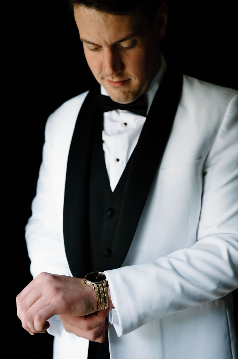 Close-up details of white tuxedo jacket with black vest and watch.