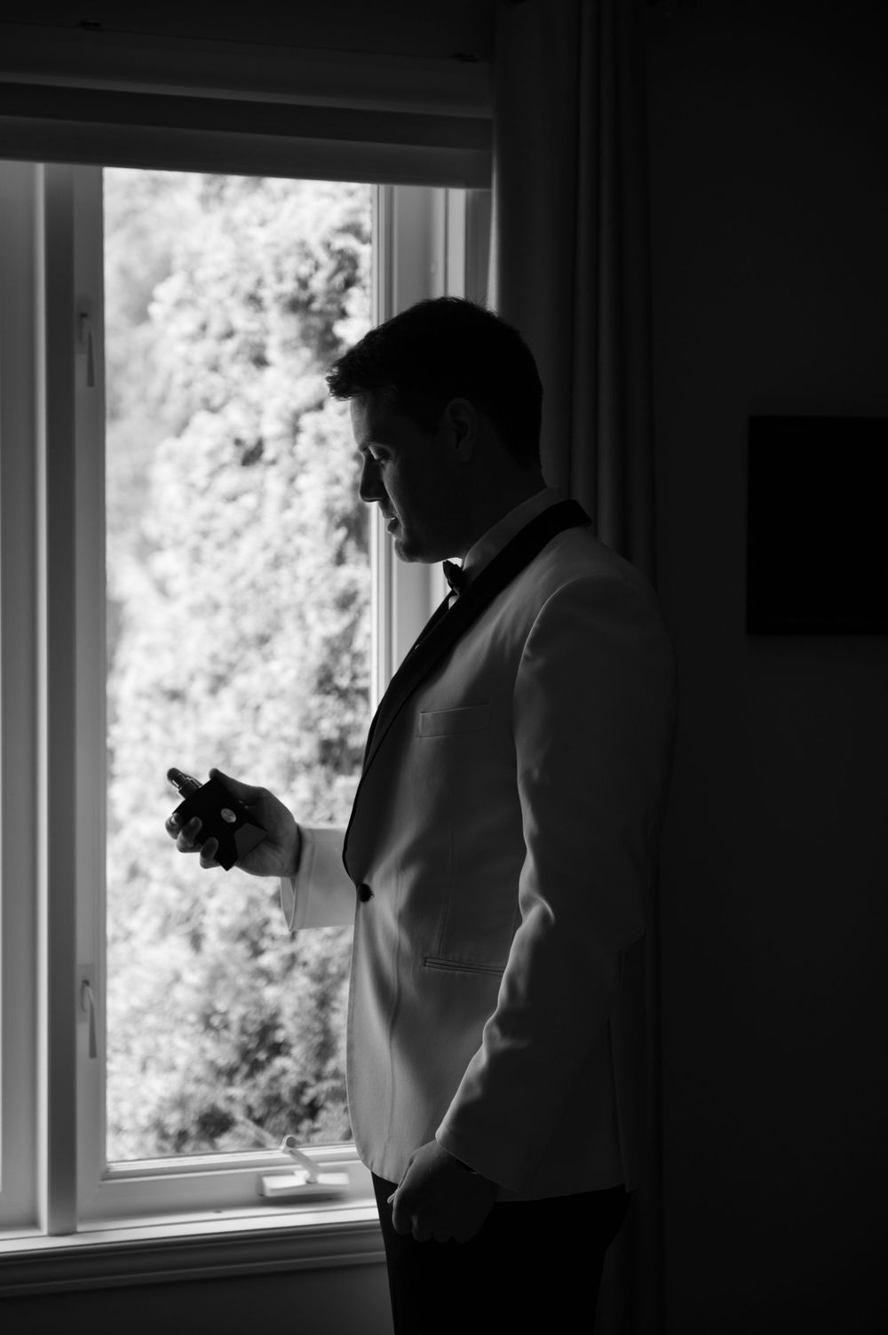 Silhouetted figure looks out bright window in dark interior room.