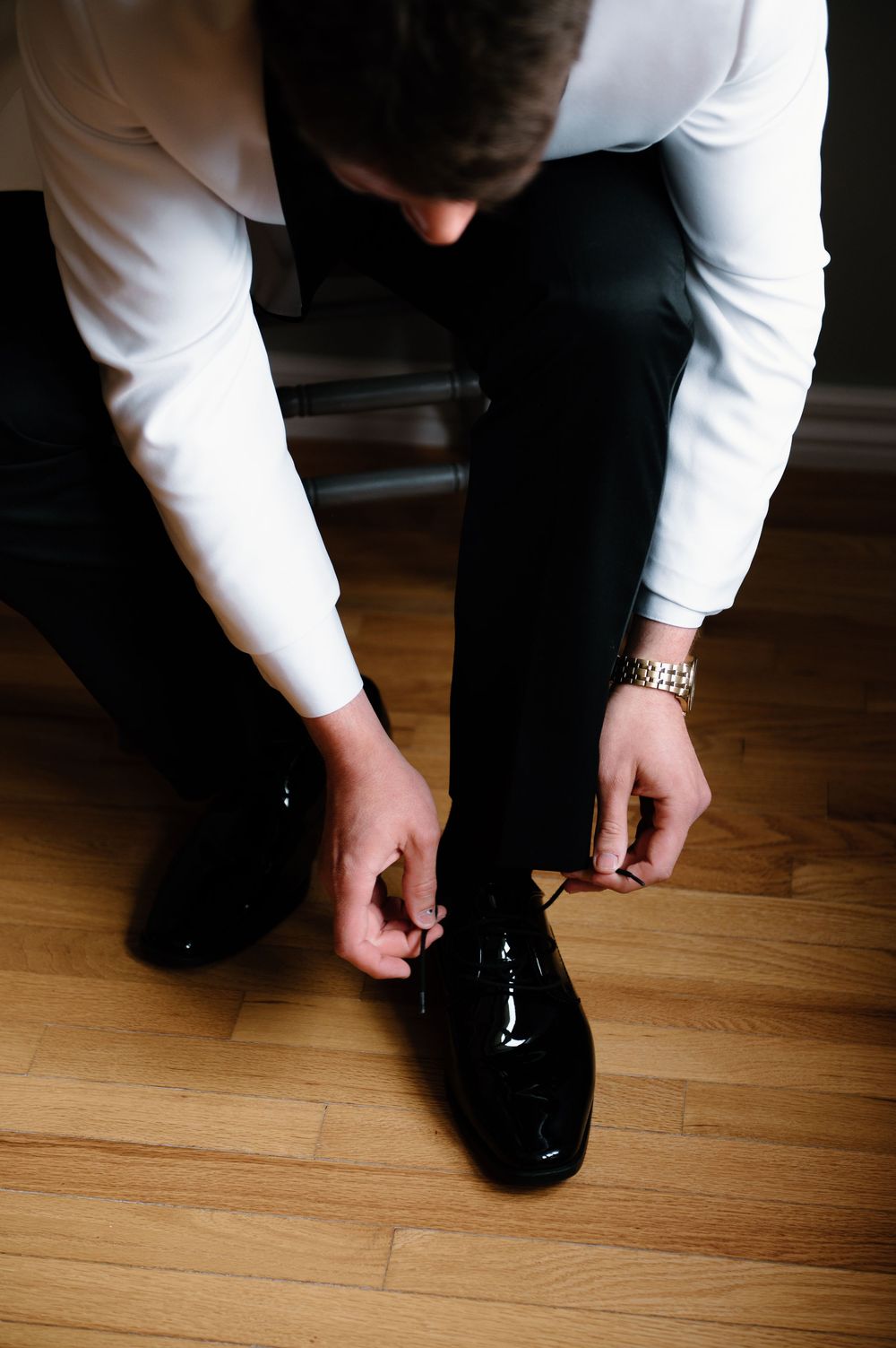 Hands adjusting formal black dress shoes on wooden floor.