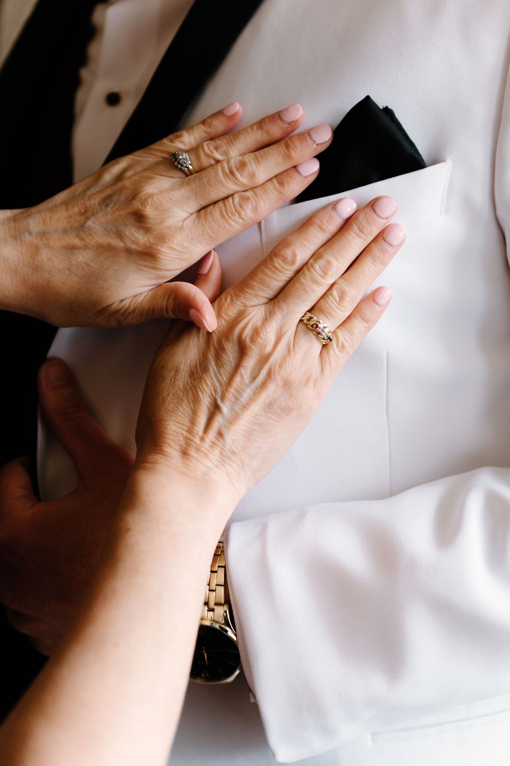 Hands with rings shown against white fabric in close-up detail shot.