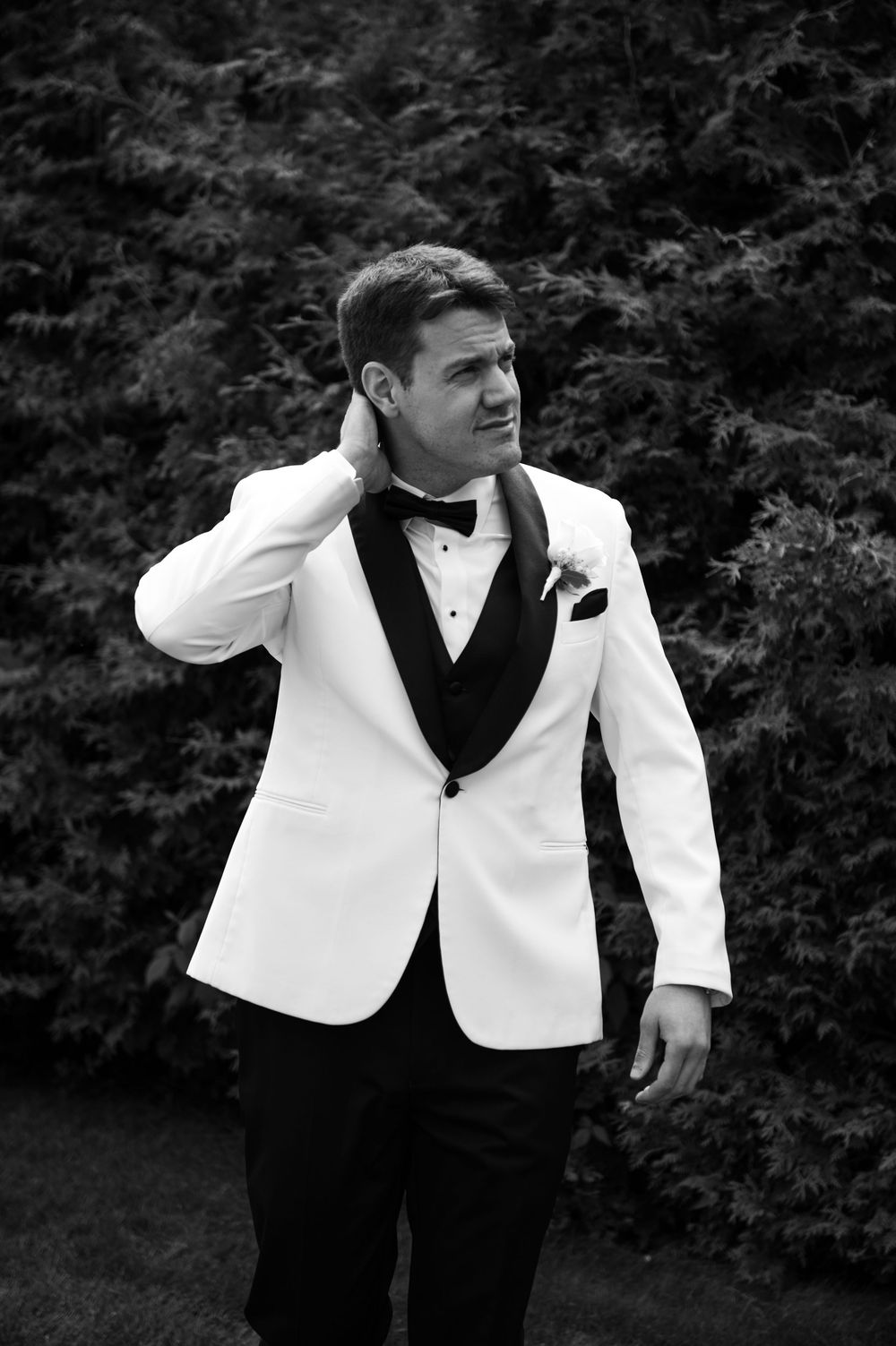 Groomsmen in black and white formal wear pose dramatically in a garden setting.